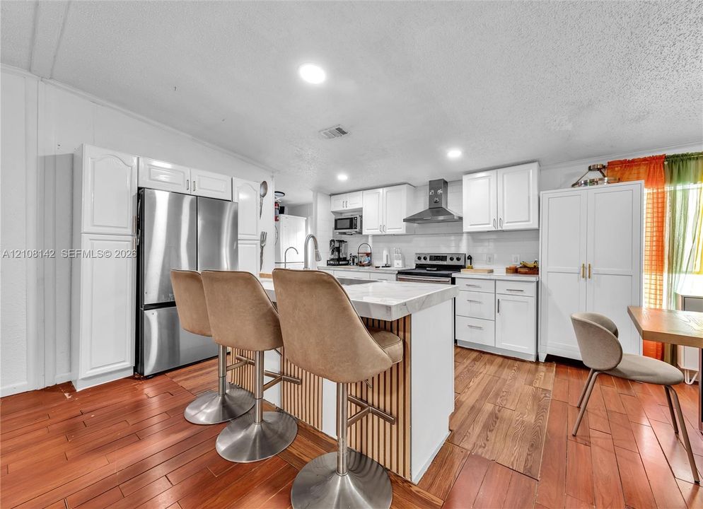 Kitchen featuring white cabinetry, wood-finish flooring, a central island with a stone-top surface and slatted wood detailing, stainless steel appliances, and a range hood