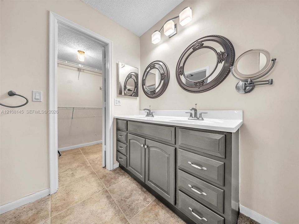 Dual-sink vanity with grey cabinetry, stone-finish countertop, tile flooring, and integrated three-light fixture