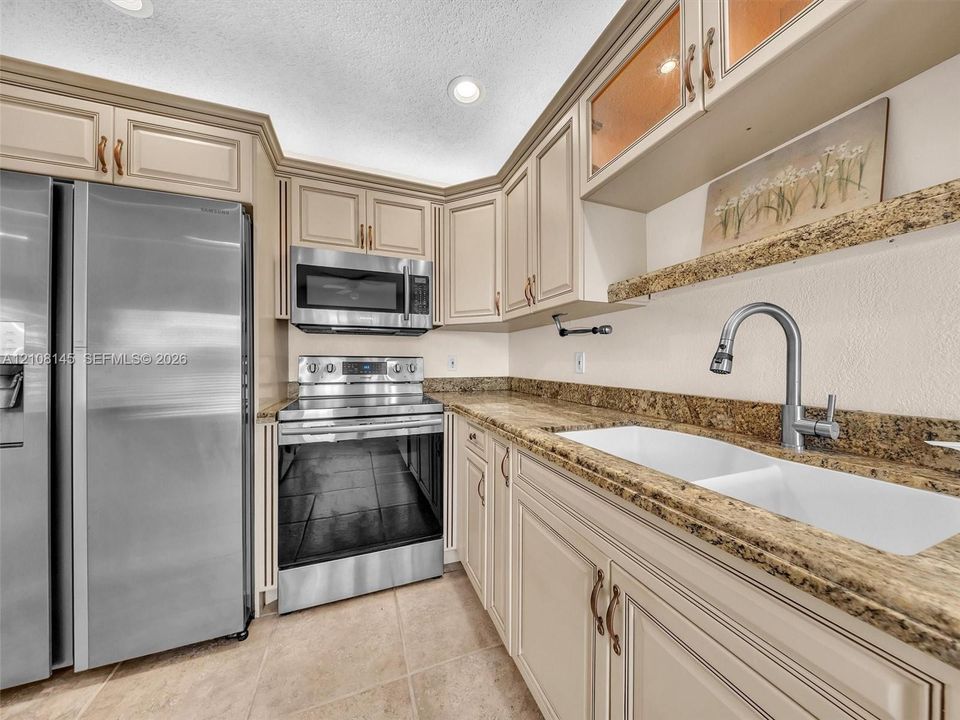 Kitchen featuring cream-colored shaker-style cabinetry, stone-finish countertops, stainless steel appliances, a dual-basin white sink with a pull-down faucet, and tile flooring