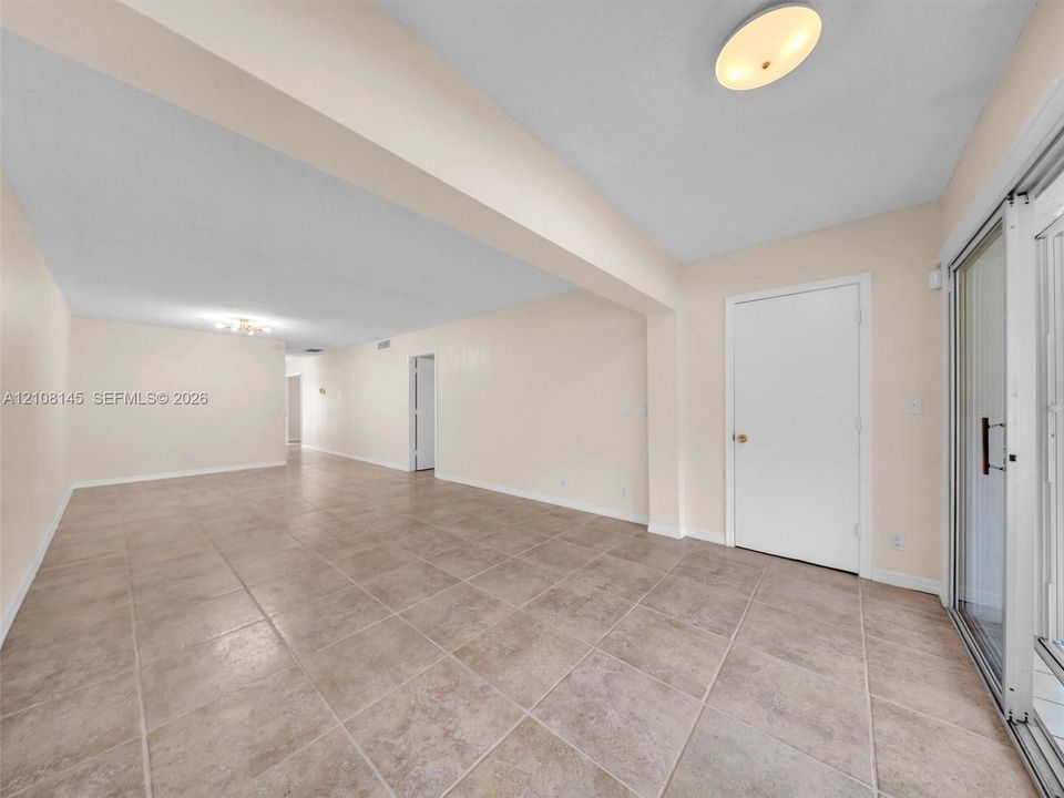Neutral-toned tile flooring, recessed architectural beam, flush-mount ceiling lighting, and glass sliding door