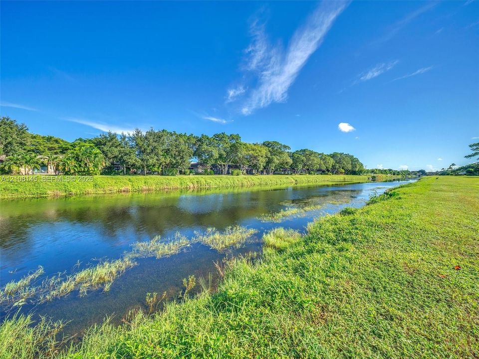 Waterfront property featuring a canal, expansive grassy lawn, and mature trees
