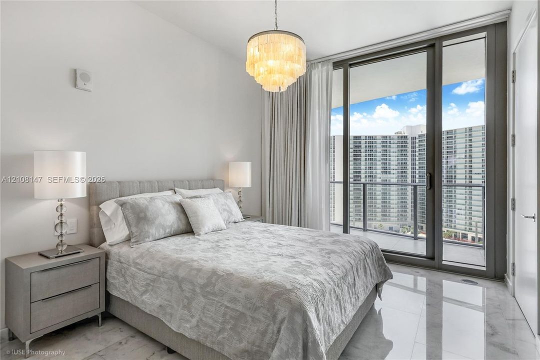 Floor-to-ceiling glass sliding doors, stone-finish tile flooring, and a tiered decorative chandelier