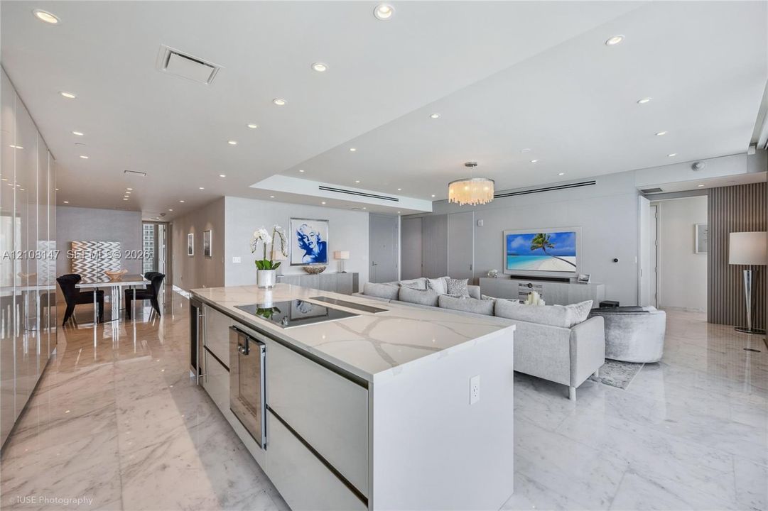 Open-concept interior featuring large-format stone flooring, recessed ceiling lighting, and a central kitchen island with integrated cooktop and built-in dishwasher