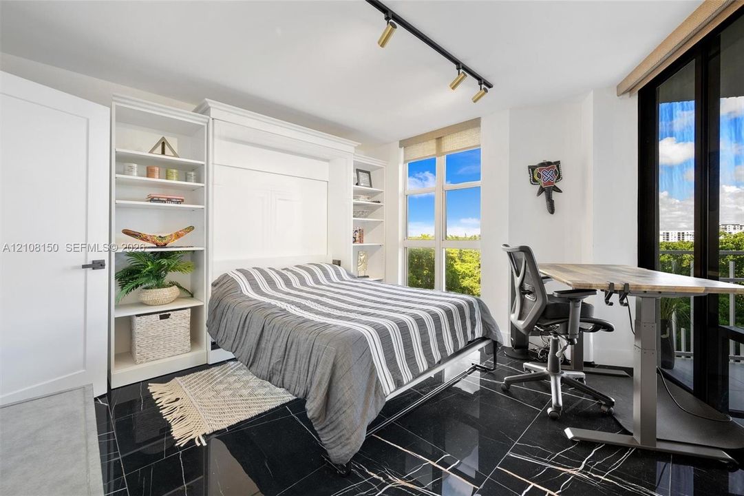 Built-in floor-to-ceiling white shelving, integrated wall bed system, black tile flooring with veining, track lighting, and full-height windows