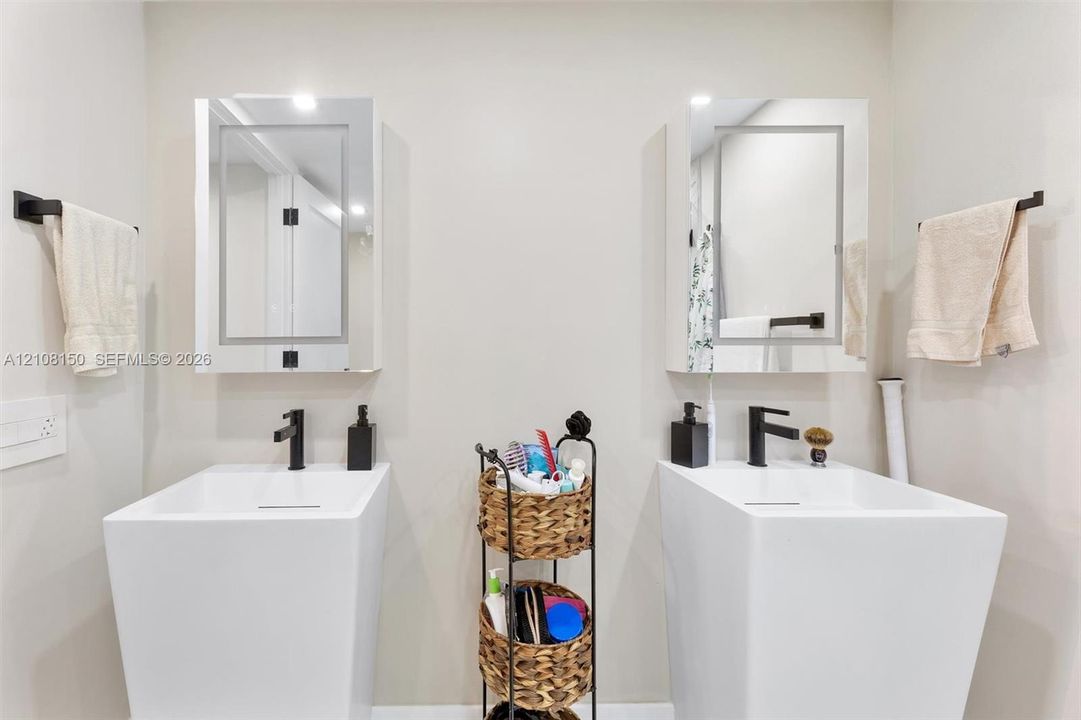 Dual pedestal sinks featuring rectangular basins and matte black faucets, paired with mirrored medicine cabinets and matte black hardware
