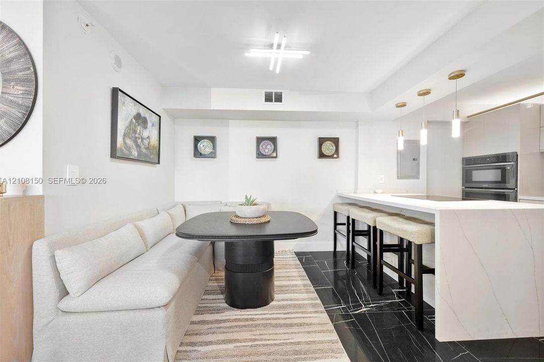 Kitchen featuring a stone-surface waterfall island, black tile flooring with white veining, built-in dual ovens, and trio of pendant lights