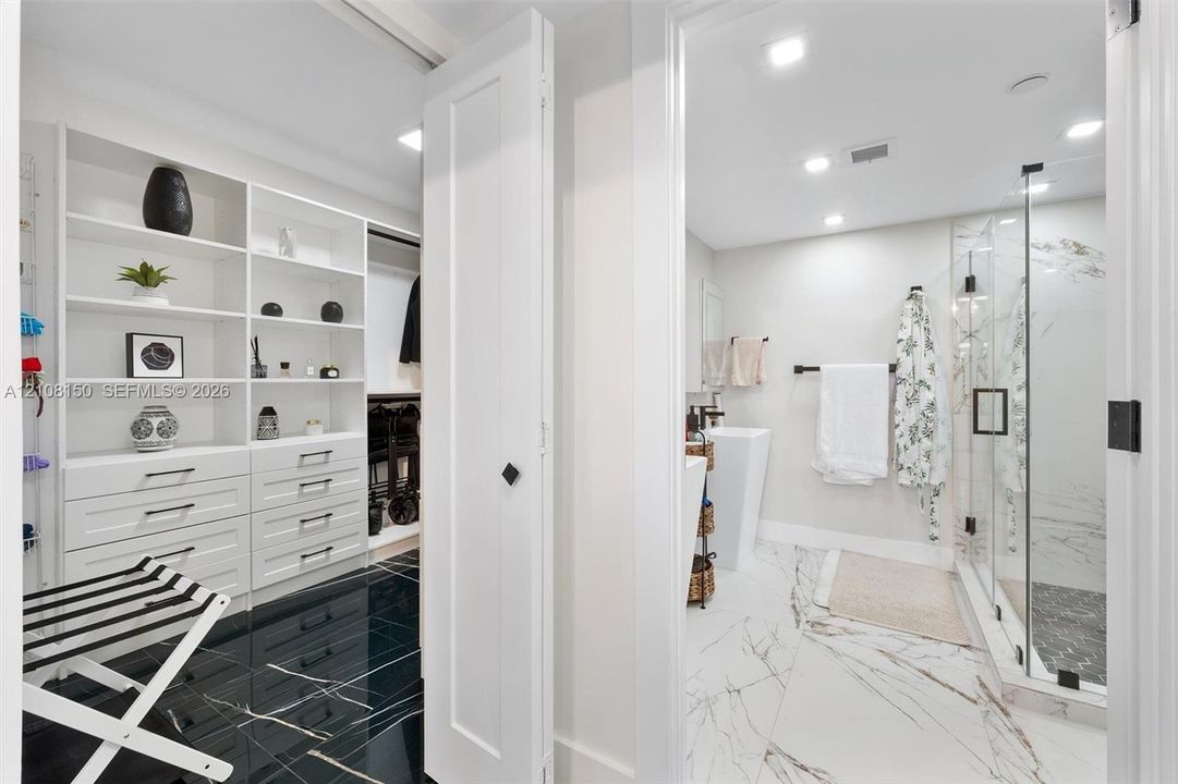 Walk-in closet featuring white built-in shelving and drawer cabinetry, complemented by high-gloss dark stone-finish flooring