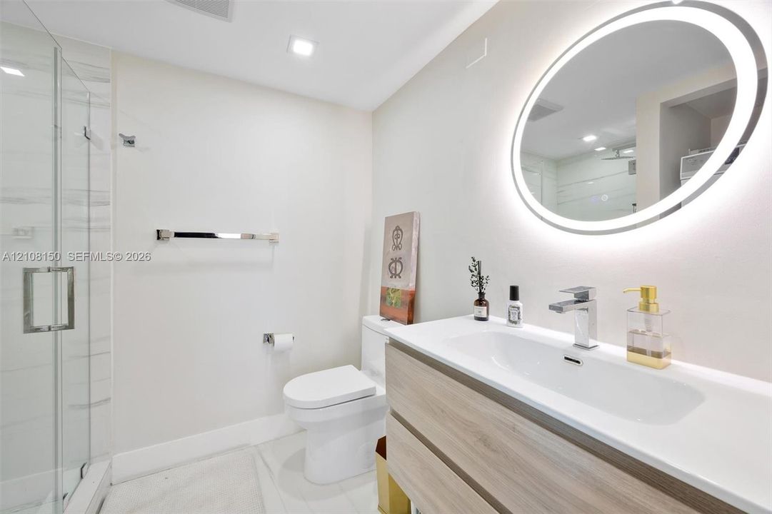 Bathroom featuring a wall-mounted vanity with wood-finish cabinetry, an integrated sink with a chrome faucet, a backlit oval mirror, and a walk-in glass shower enclosure