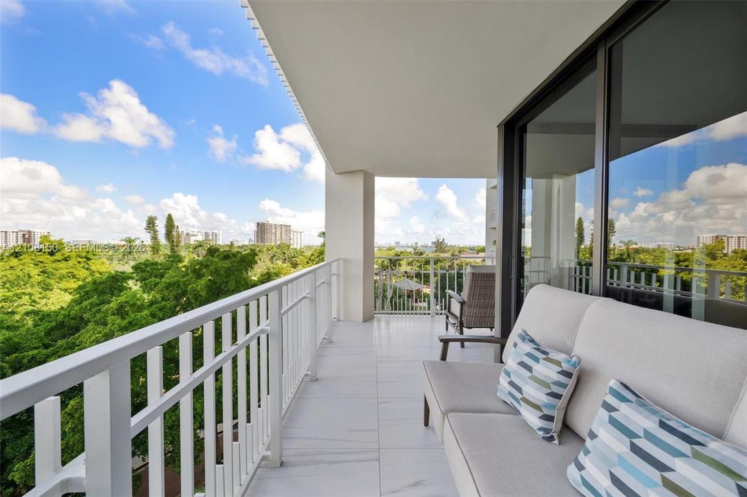 Covered balcony featuring large-format porcelain tile flooring, white metal railing, and floor-to-ceiling glass sliding doors