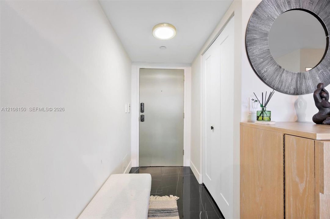 Entryway featuring polished dark stone flooring, high-gloss finish entry door with electronic keypad, and floor-to-ceiling built-in closet with dual doors