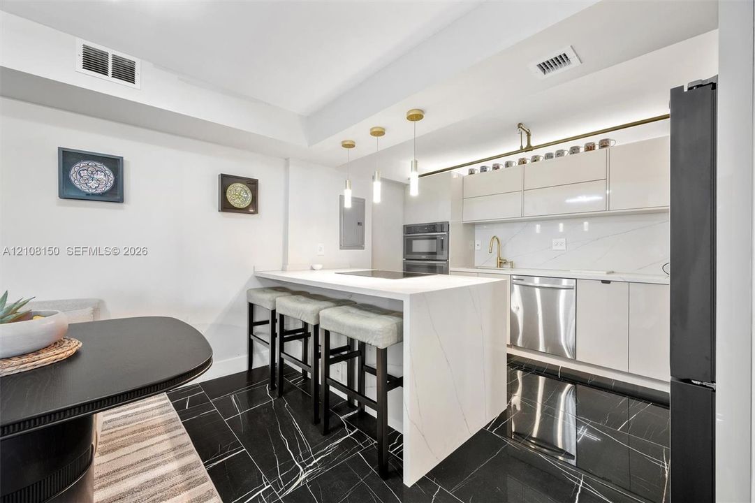 Kitchen featuring an island with a stone-finish waterfall edge, high-gloss cabinetry, stainless steel appliances, pendant lighting, and polished stone-finish flooring