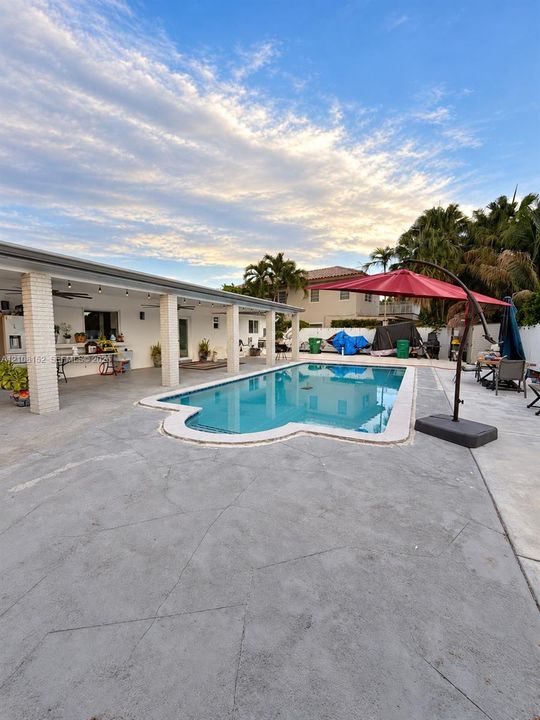 In-ground swimming pool with a curved edge, expansive concrete patio, and a covered lanai featuring brick-pillar supports