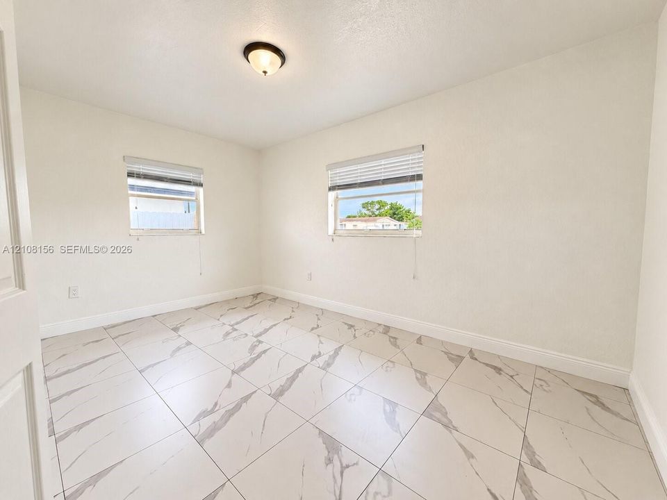 Room featuring large-format tile flooring with veining, two windows with horizontal blinds, and a centered flush-mount light fixture