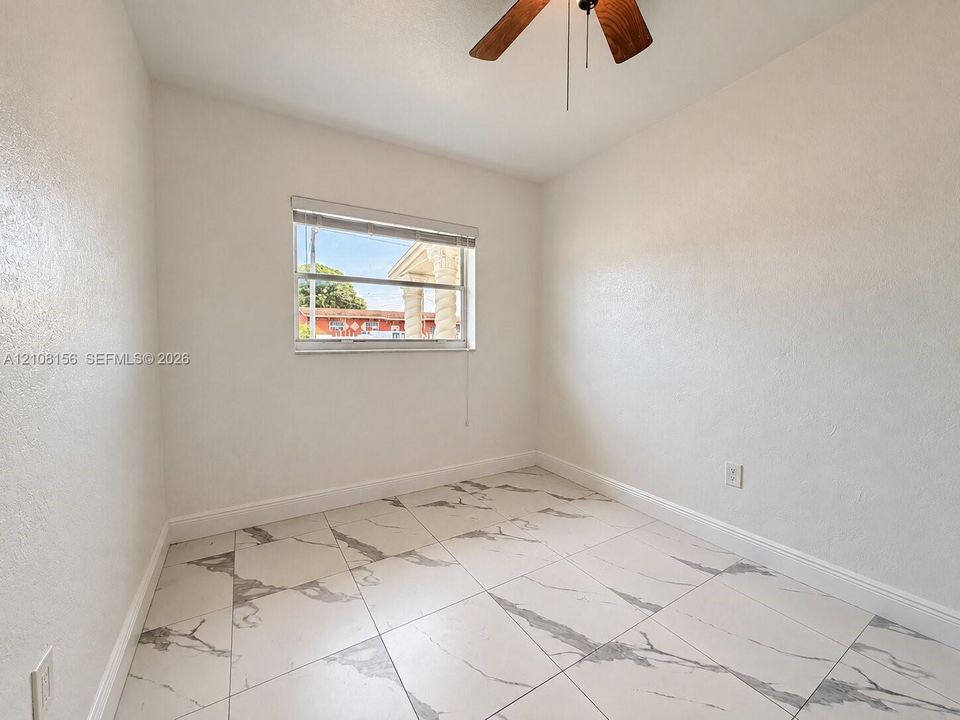 Room featuring large-format tile flooring with a neutral veined pattern, smooth wall finishes, a single-hung window, and a ceiling-mounted fan with wood-finish blades