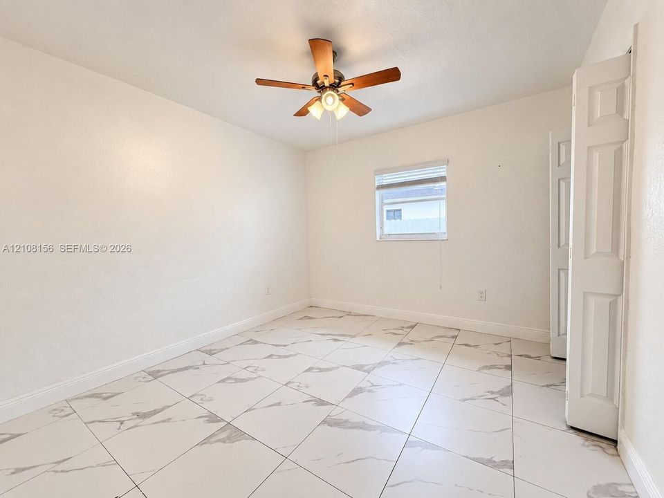 Interior room featuring large-format tile flooring with a neutral pattern, high-contrast ceiling fan with integrated lighting, and white six-panel closet doors