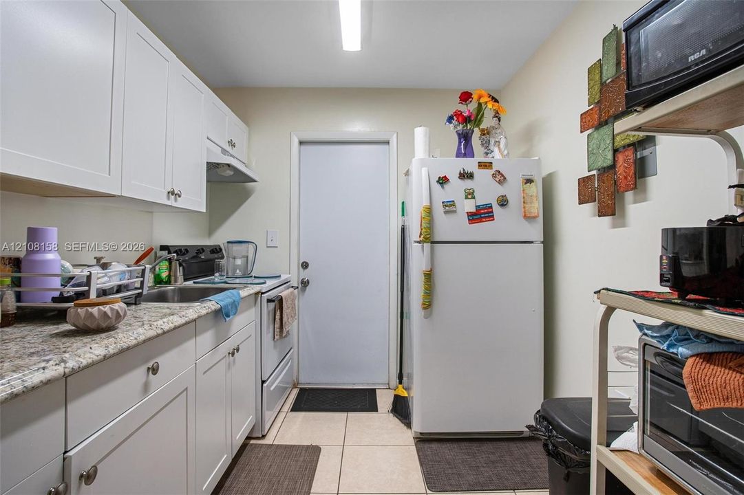 Kitchen featuring white cabinetry, stone-finish countertops, stainless steel sink, and tile flooring
