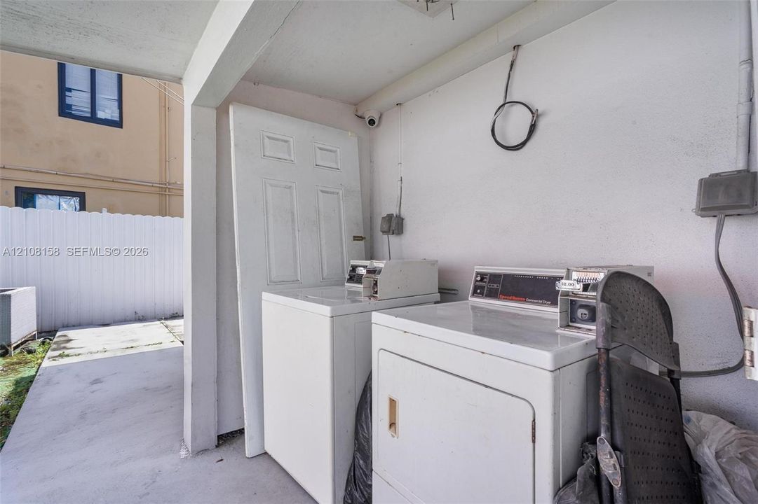 Covered concrete utility area featuring painted masonry walls and coin-operated laundry equipment