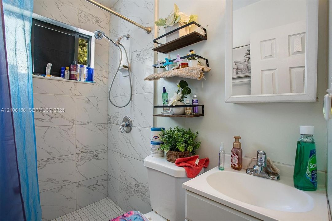 Bathroom featuring floor-to-ceiling stone-patterned tile, white vanity with integrated oval sink, chrome-finished hardware, and recessed medicine cabinet