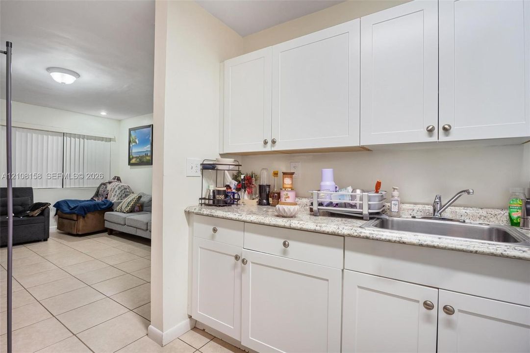 Kitchenette featuring white cabinetry, stone-patterned countertops, stainless steel sink with a metallic faucet, and tile flooring