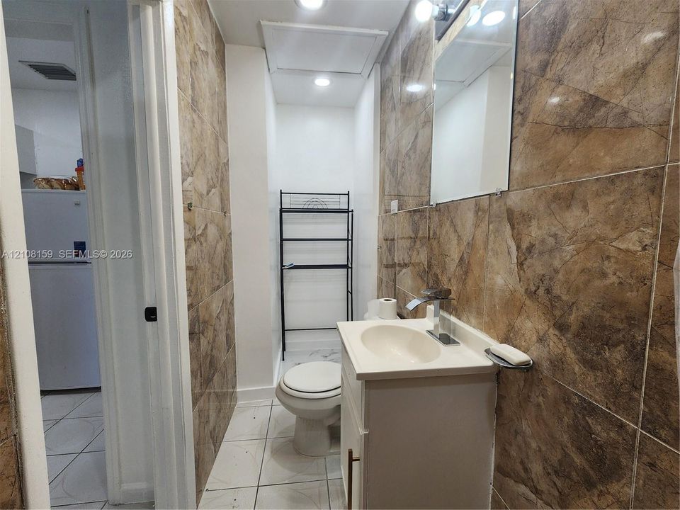 Bathroom featuring floor-to-ceiling stone-patterned wall tile, white vanity cabinet with integrated sink, chrome faucet, and recessed lighting