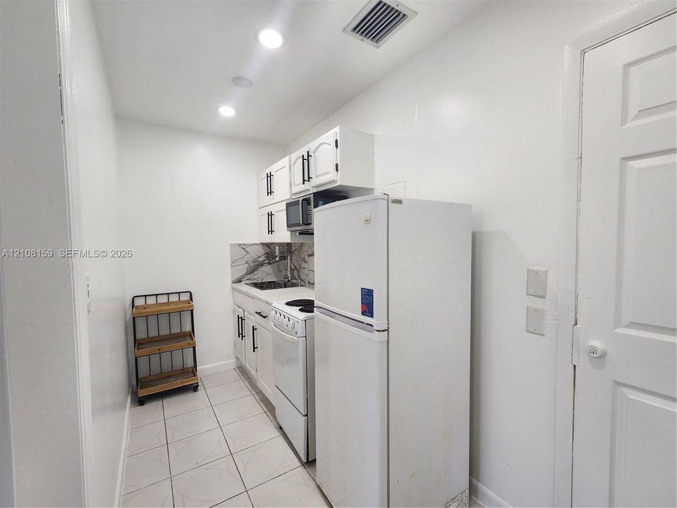 Kitchen featuring white cabinetry with matte black hardware, stone-finish backsplash, built-in range, and tile flooring