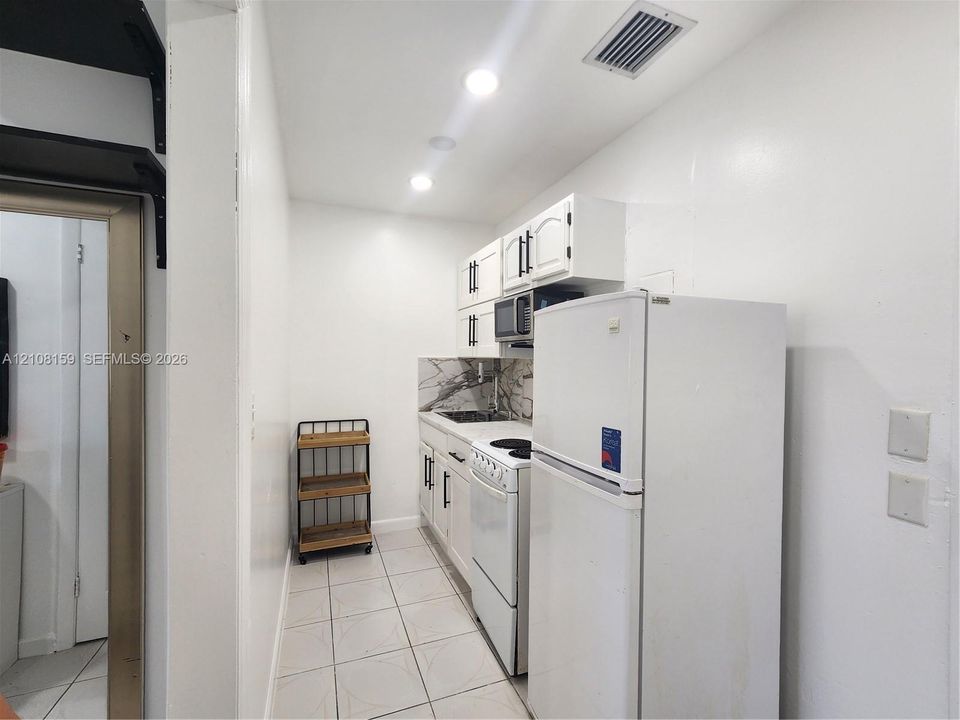 Kitchen featuring white cabinetry with dark hardware, patterned stone-finish backsplash, recessed lighting, and tile flooring