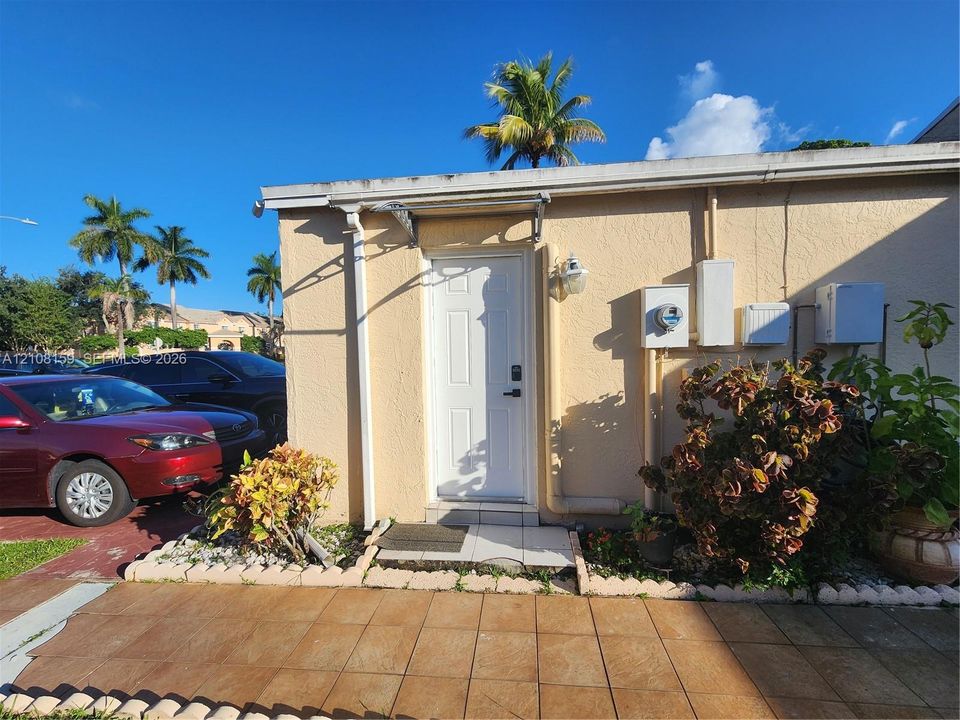 Stucco exterior featuring a white paneled door with overhead awning, tiled patio, and manicured landscaping