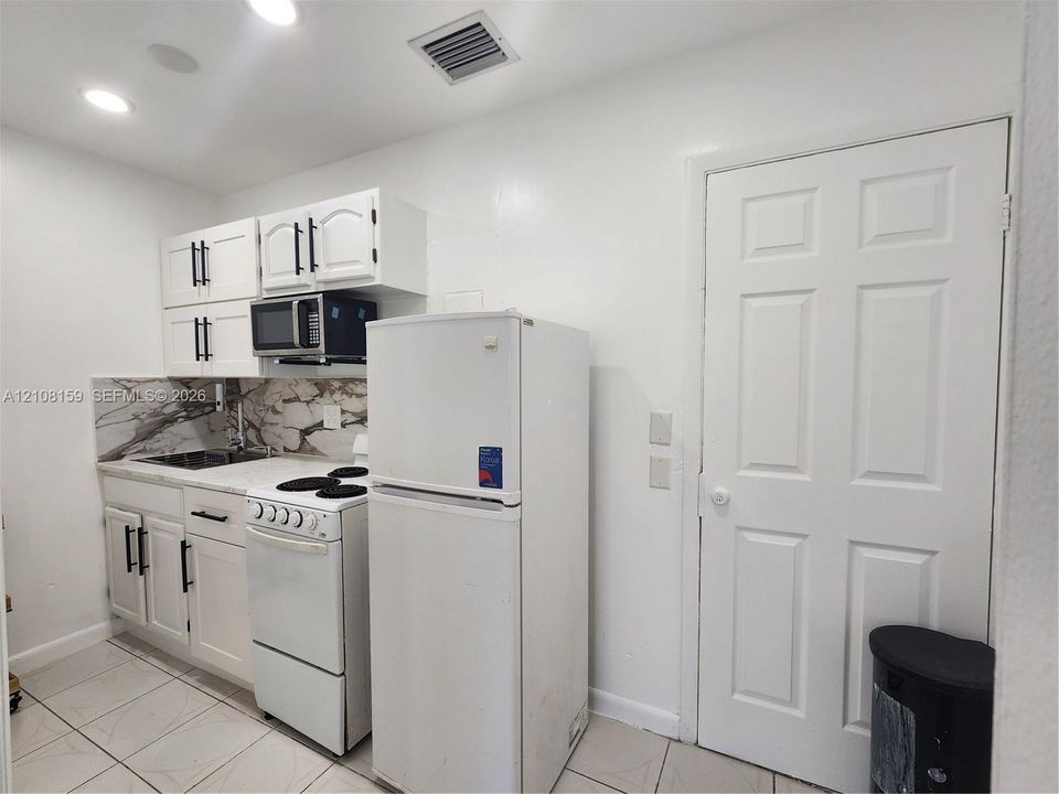 Kitchenette featuring white cabinetry with dark hardware, stone-finish backsplash, built-in microwave, and tile flooring