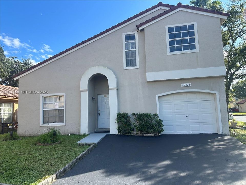 Two-story exterior featuring a stucco facade, tiled roof, arched entryway, and an attached single-car garage