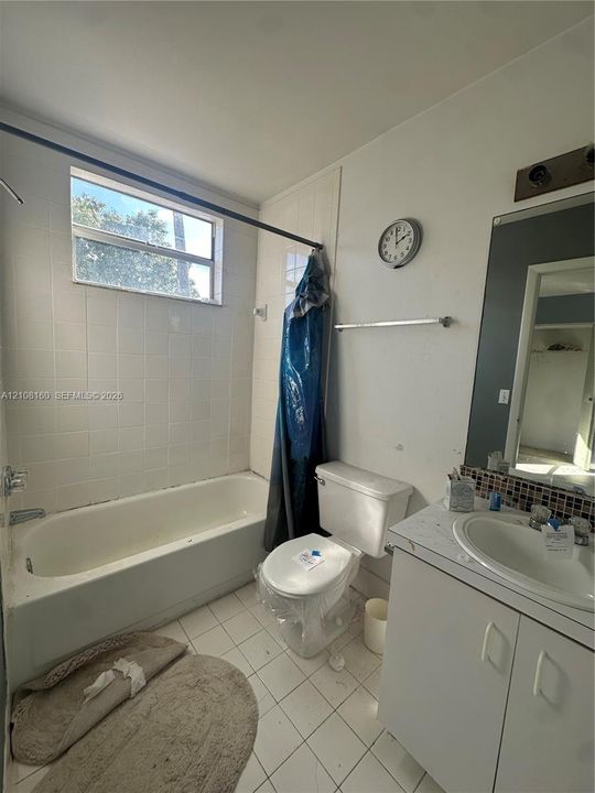Bathroom featuring white tiled tub surround, rectangular window, vanity with integrated basin, mosaic tile backsplash, and wall-mounted vanity mirror