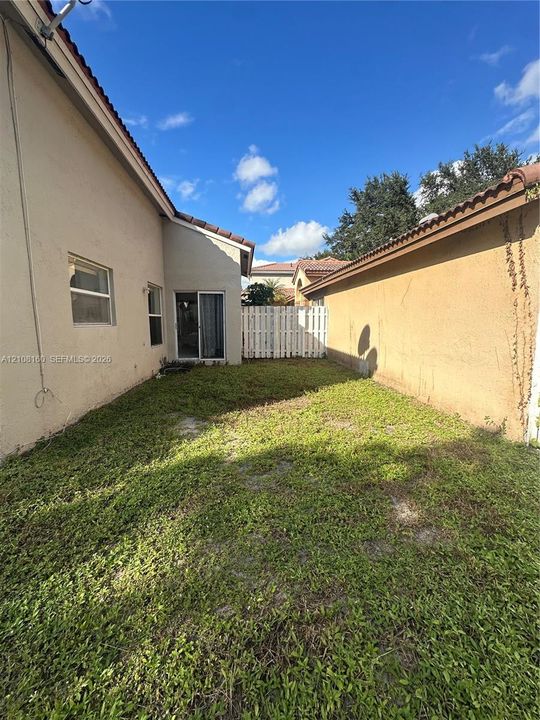 Side yard exterior featuring stucco siding, tile roofline, sliding glass door, and a white privacy fence