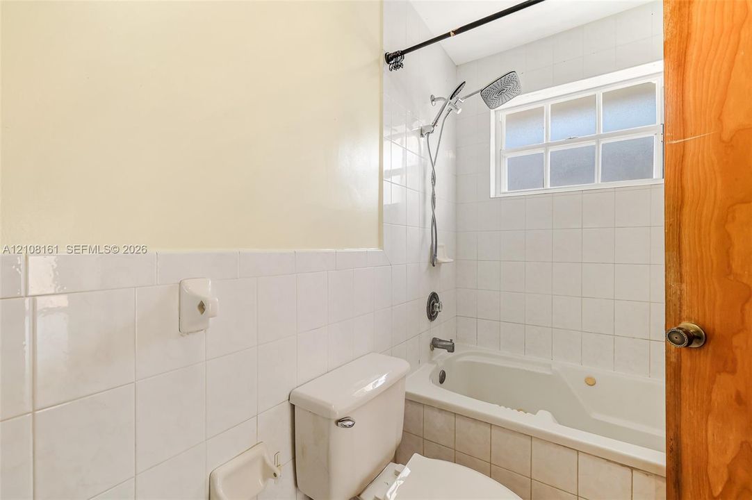 Bathroom featuring white tile wall surround, soaking tub, adjustable shower head, and a rectangular window