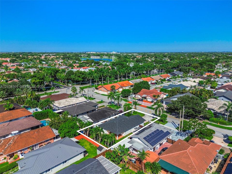 Aerial perspective of a residential lot featuring a multi-hipped roofline, mature palm trees, and fenced perimeter