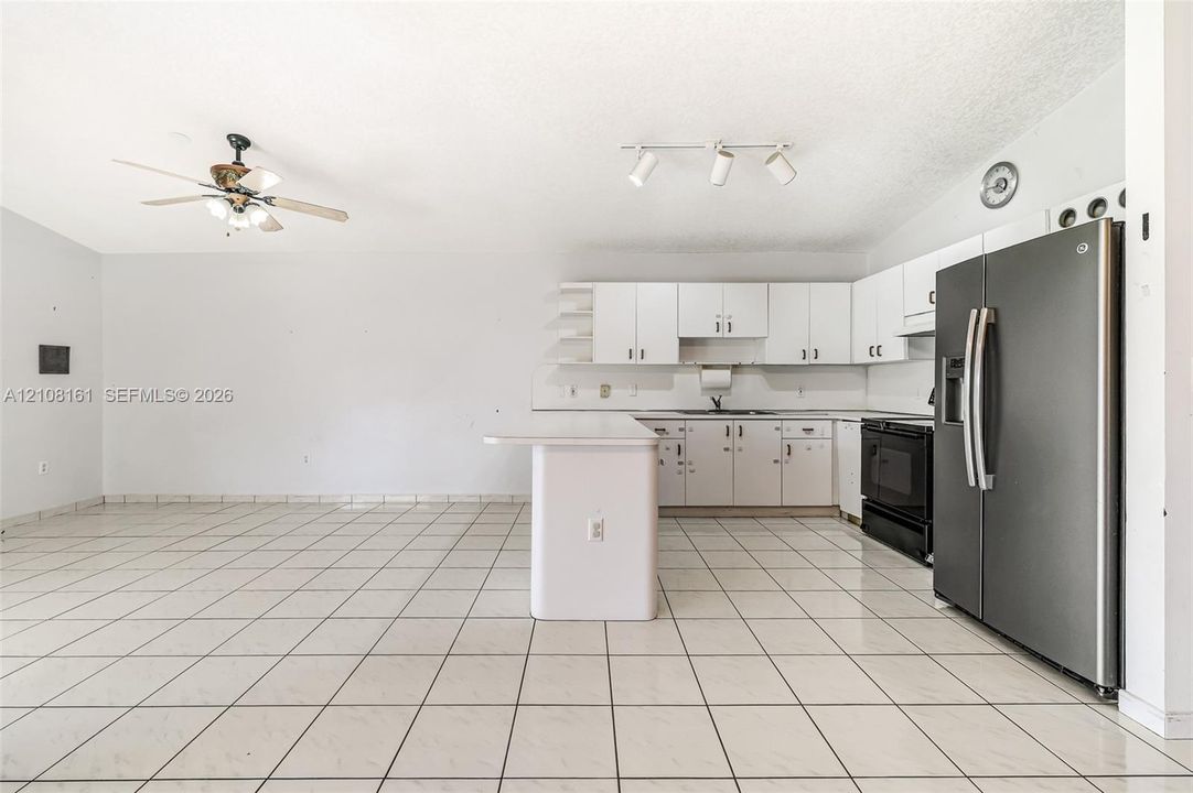 Kitchen featuring white cabinetry, an island with an extended countertop, large-format tile flooring, a stainless steel side-by-side refrigerator, and track lighting
