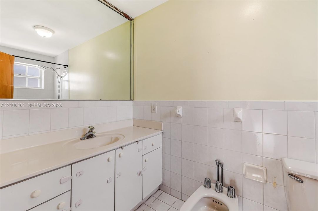 Bathroom featuring a white vanity with an integrated sink, a full-width wall mirror, white wall tiling, and a bidet