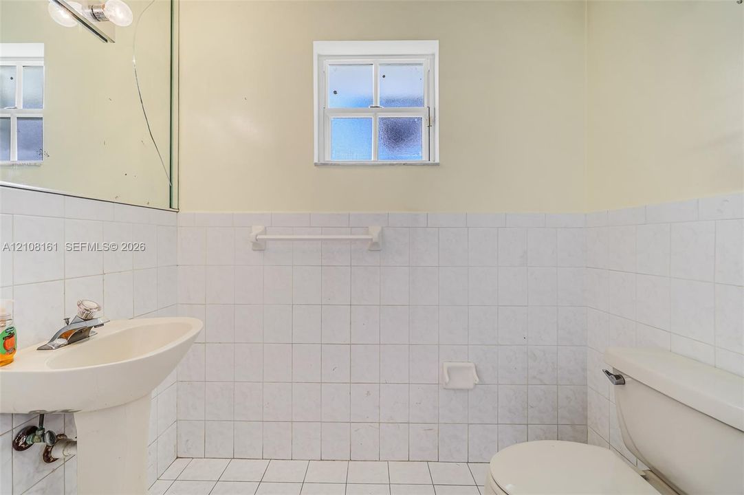 Bathroom featuring a pedestal sink with a chrome faucet, white square-tile wainscoting, a multi-pane fixed window, and a built-in ceramic soap dish