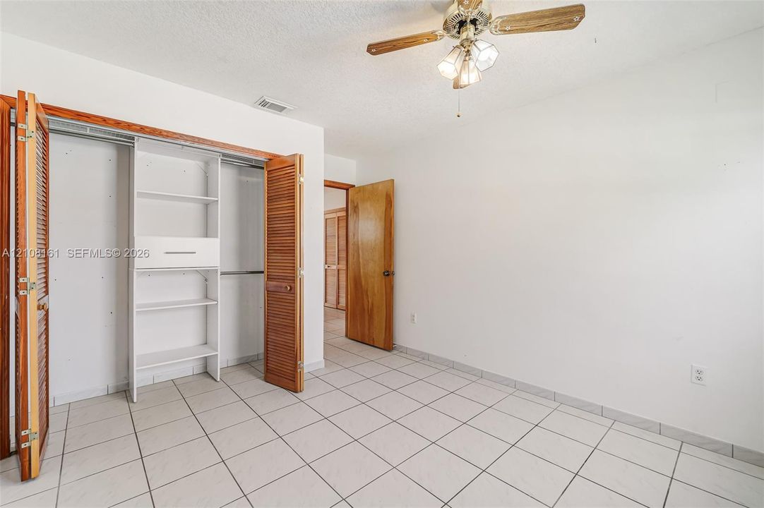 Room featuring ceramic tile flooring, a dual-door closet with built-in shelving, a natural wood-finish interior door, and a multi-light ceiling fan