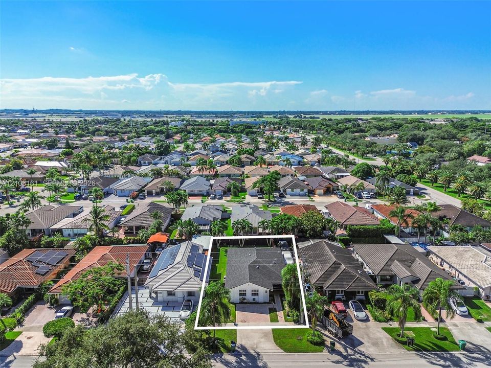 Aerial perspective of a single-story residence featuring a hipped roof, paved driveway, brick-paver entryway, and mature palm landscaping