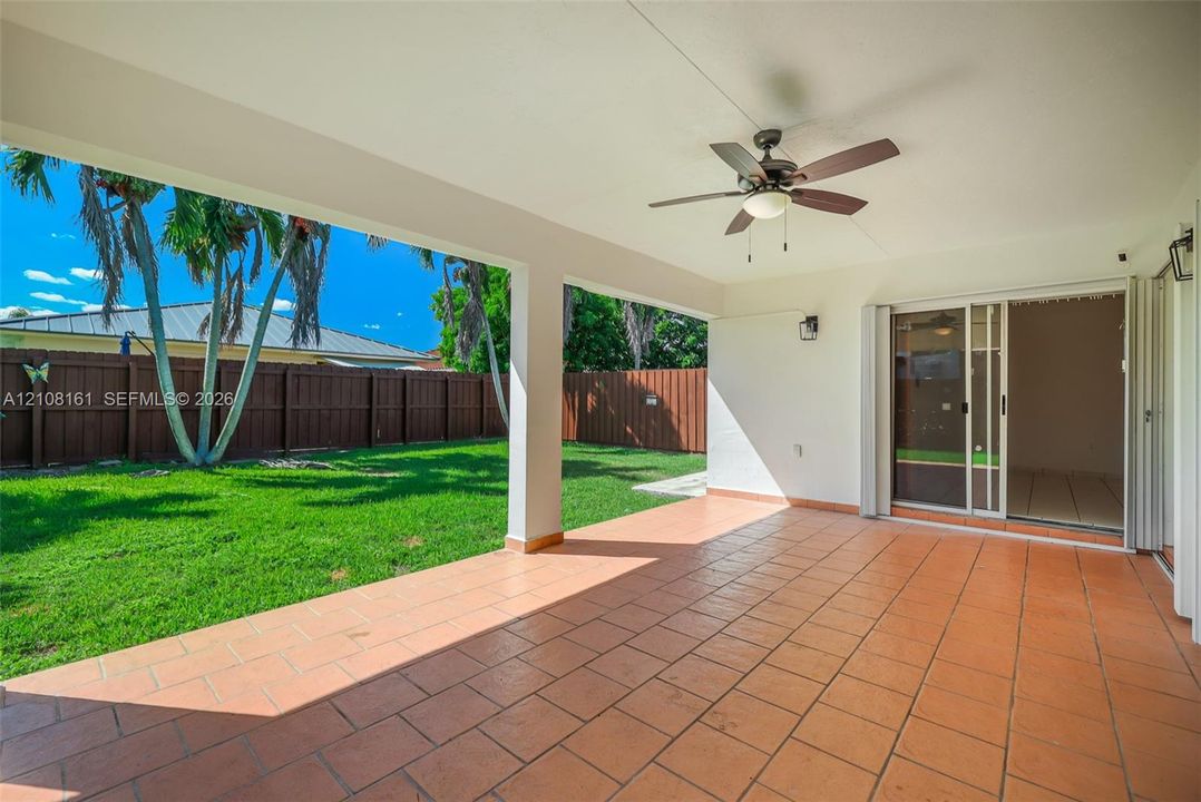 Covered patio featuring ceramic tile flooring, a ceiling fan, sliding glass doors, and a fenced backyard