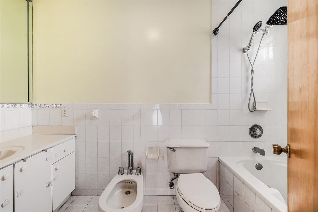 Bathroom featuring a white vanity cabinet, ceramic tile walls, a porcelain bidet, and a shower-tub combination with a wall-mounted rainfall showerhead