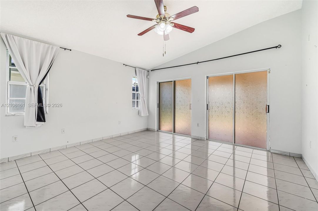 Vaulted ceilings, large-format tile flooring, dual sets of sliding glass doors, and a central ceiling fan with integrated lighting