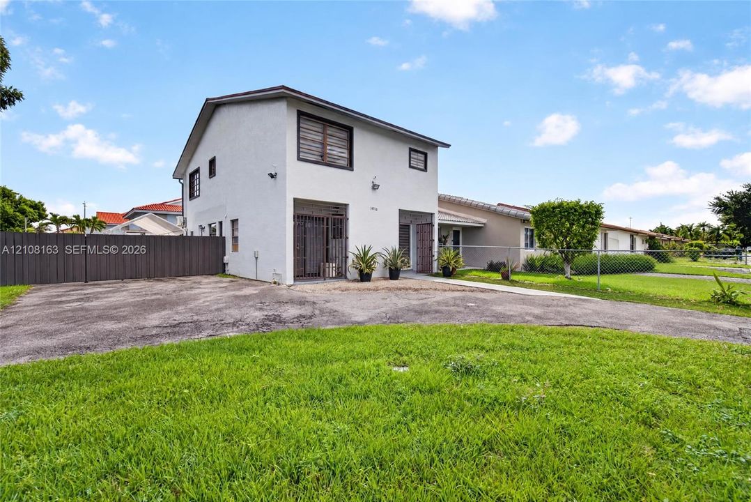 Two-story exterior featuring a light-toned stucco facade, dual ground-level entryways with metal security gates, and a paved asphalt driveway