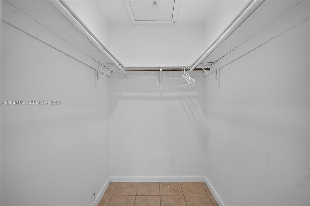 Storage area featuring neutral tile flooring, white interior walls, and dual-level wall-mounted shelving rods