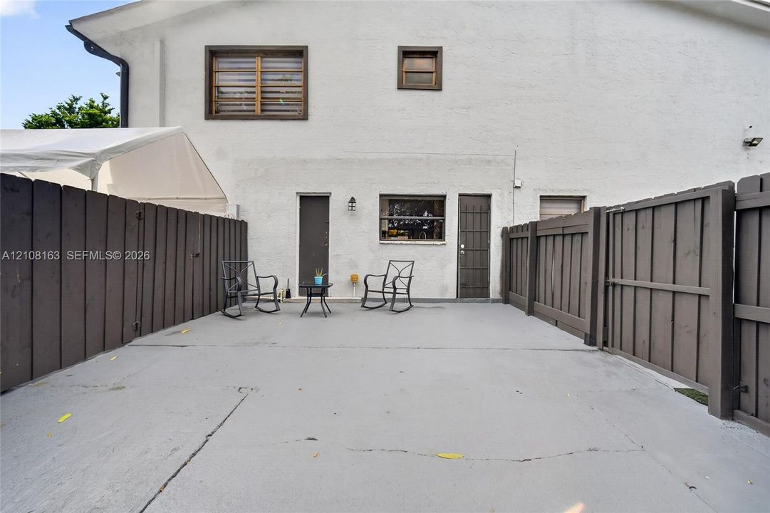 Stucco exterior featuring a concrete patio, wood-style privacy fencing, and exterior wall-mounted lighting