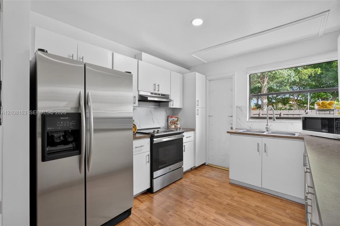 Kitchen featuring white cabinetry, stainless steel appliances, wood-finish flooring, a double-basin sink with a gooseneck faucet, and stone-finish backsplash