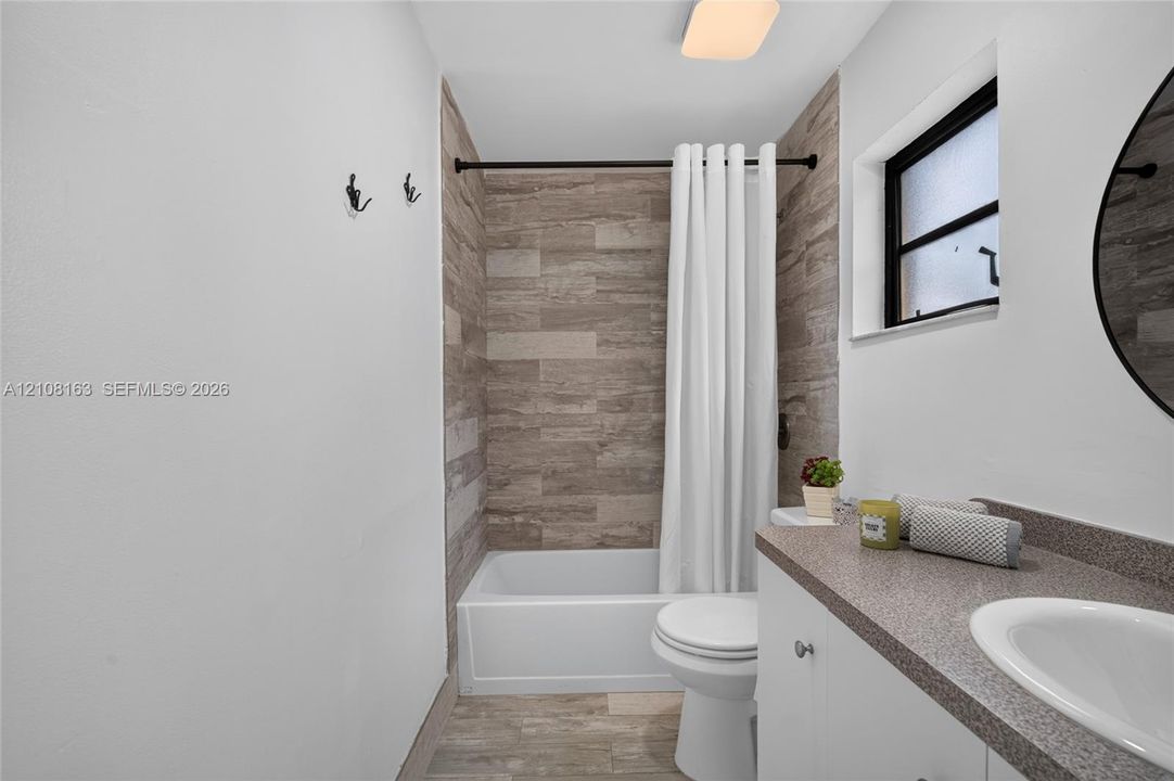 Bathroom featuring a stone-finish tile tub surround, white vanity cabinet with a stone-finish countertop, undermount sink, and wood-finish tile flooring