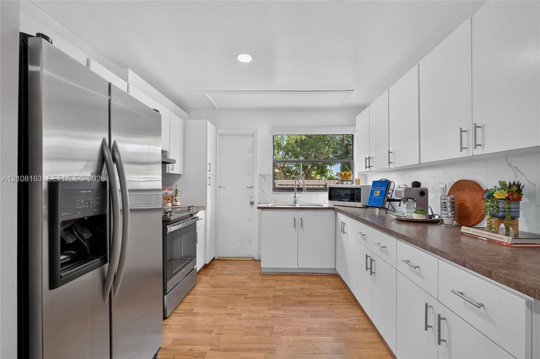 Kitchen featuring white cabinetry, wood-finish flooring, stainless steel appliances, and a rectangular undermount sink with a gooseneck faucet