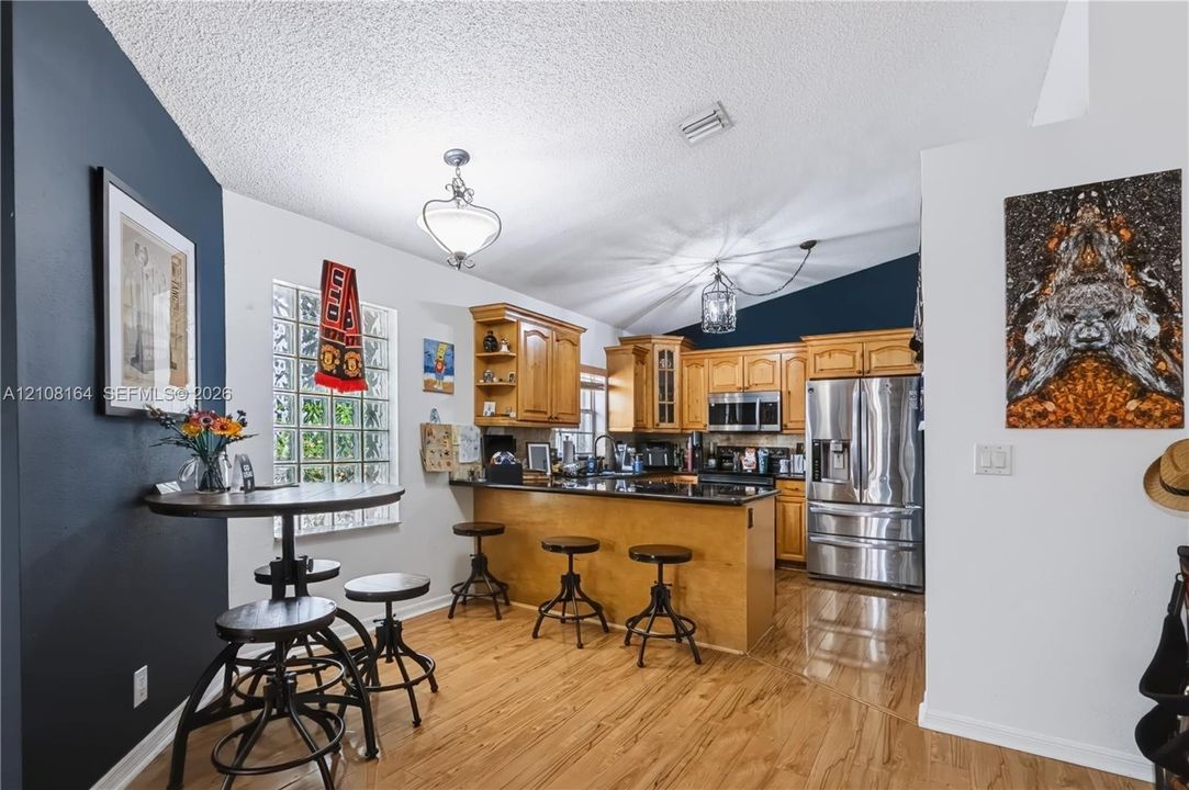 Kitchen featuring wood cabinetry, dark stone countertops, stainless steel appliances, wood-finish flooring, and a decorative glass block window