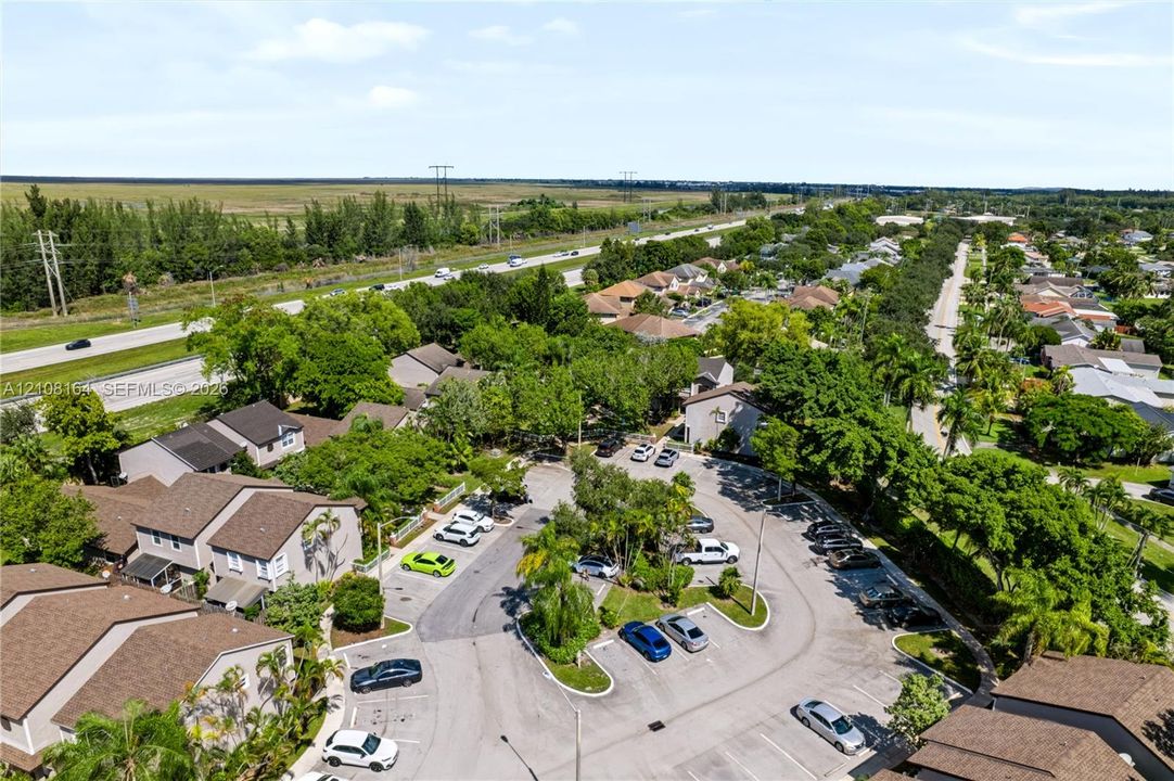 Aerial perspective of multi-family residential structures featuring shingle roofs, stucco siding, and paved surface parking