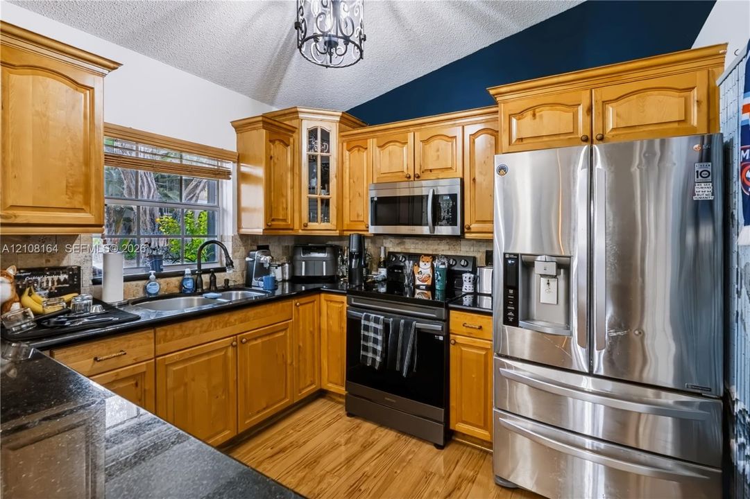Kitchen featuring wood cabinetry, stone countertops, stainless steel appliances, a vaulted ceiling with a decorative pendant light, and wood-finish flooring